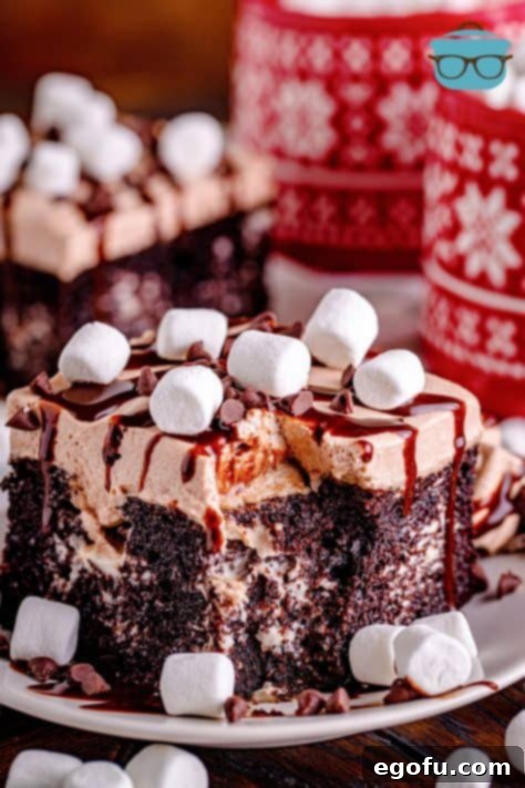 slice of hot chocolate poke cake on a white plate with two red mugs in the background.