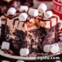 closeup photo of a slice of hot chocolate poke cake topped with mini marshmallows on a white plate.