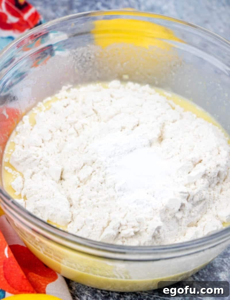 Starbucks Zesty Lemon Loaf 8 All-purpose flour is added to the lemon loaf batter in a clear bowl, ready to be gently mixed.