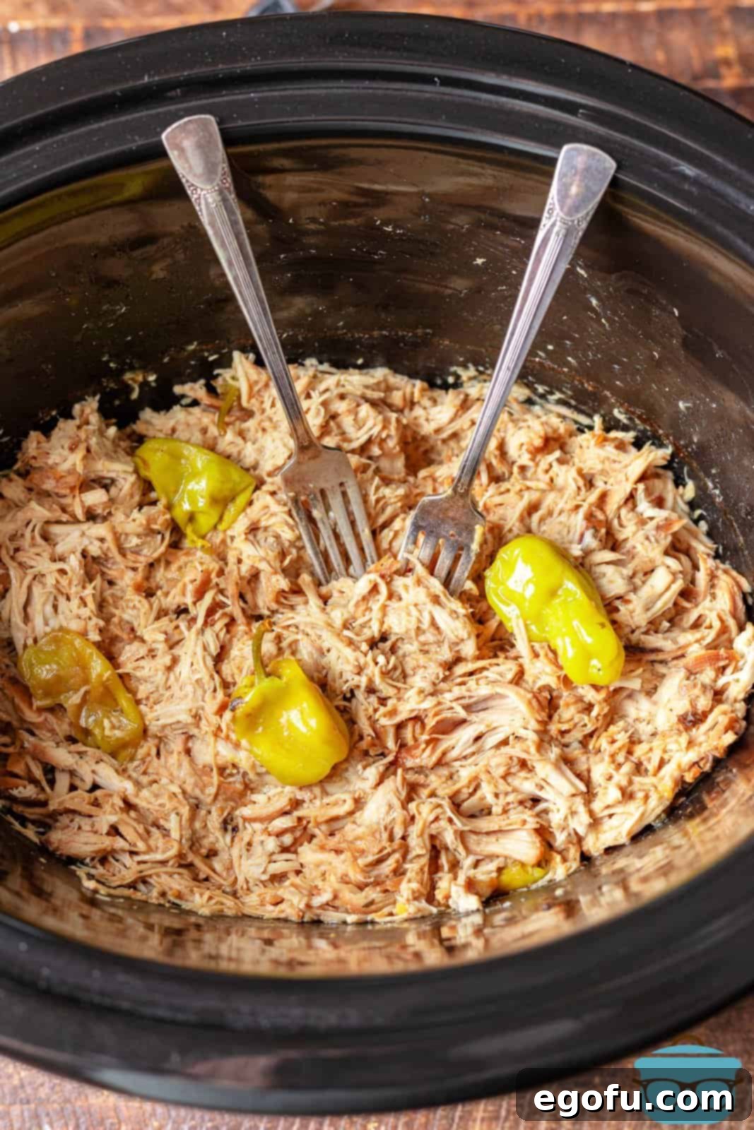 two forks in shredded chicken in a slow cooker.