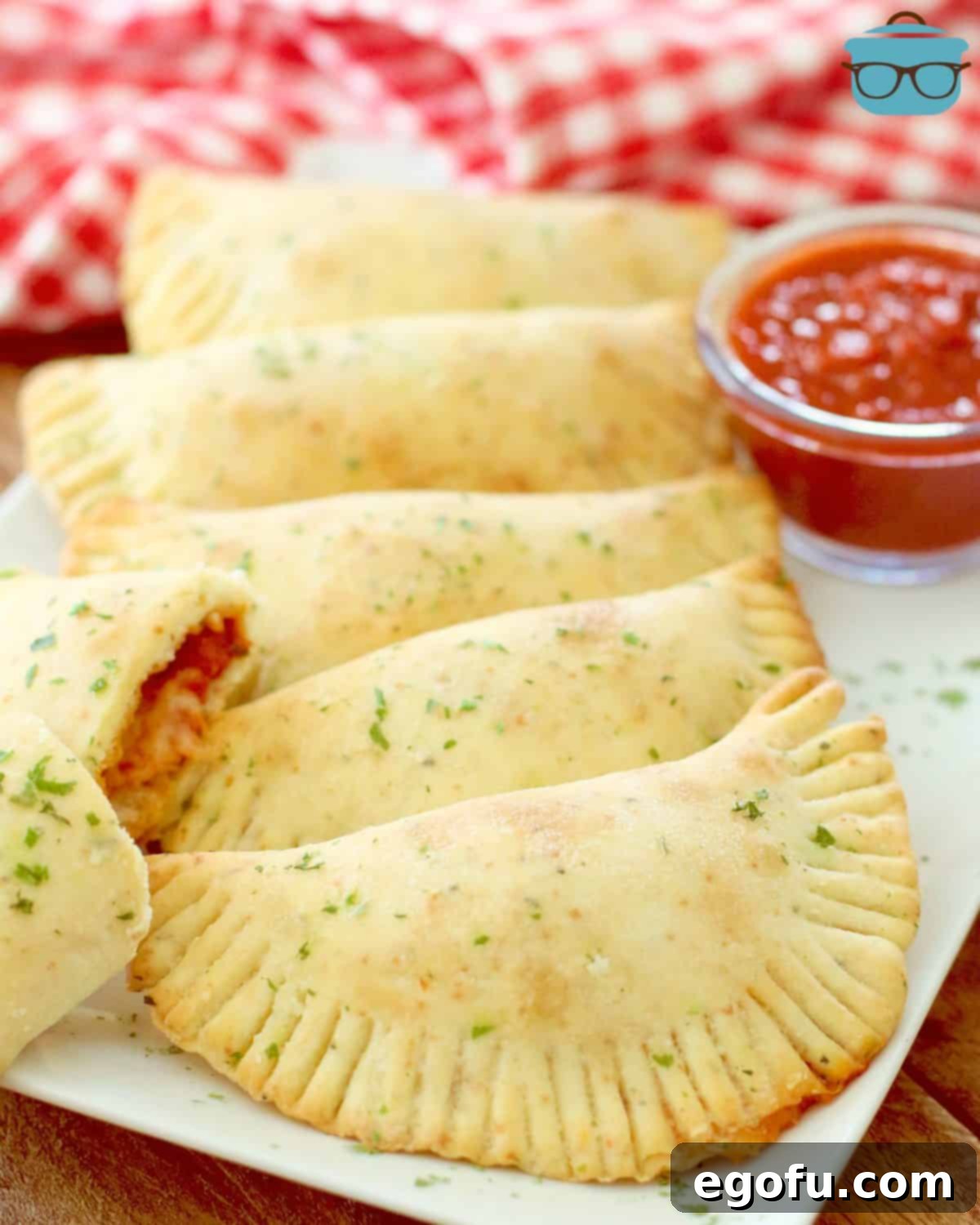 Homemade Pizza Pockets laid out on a white platter with a side of pizza sauce for dipping.