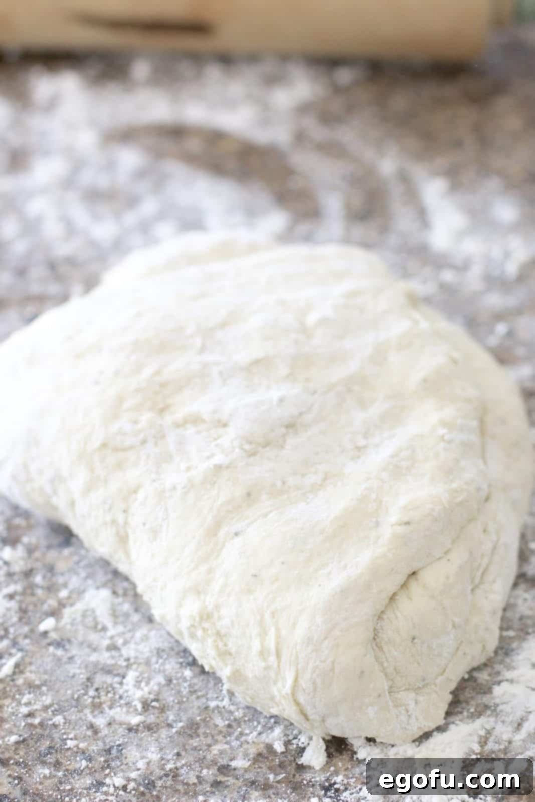 Pizza dough being kneaded on a floured surface, hands visible in the process.