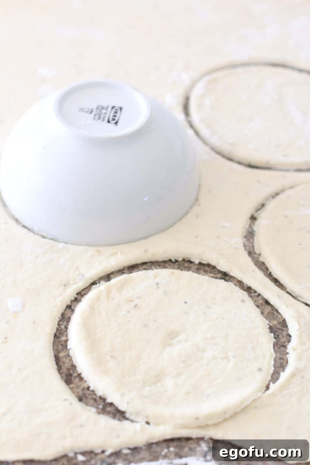 A small white bowl being used to cut out circular shapes from the flattened pizza dough.
