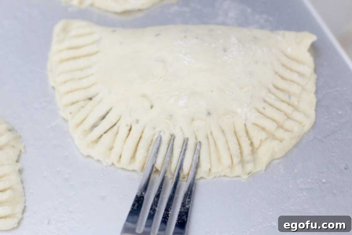 A fork crimping the edges of a filled pizza pocket on a baking sheet, creating a sealed seam.