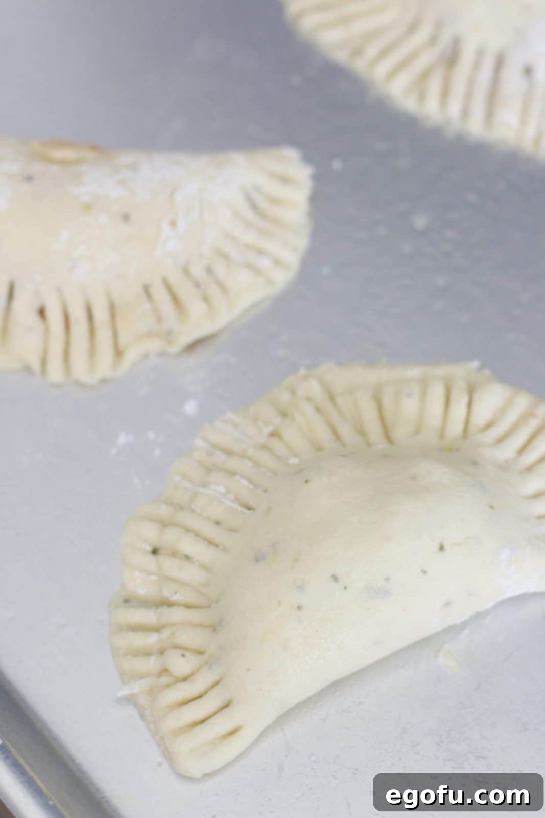 Uncooked pizza pockets shown on a baking sheet, with crimped edges, ready to be baked to golden perfection.