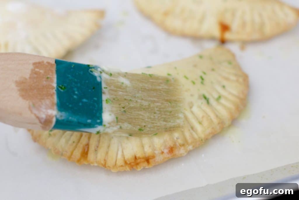 Melted butter being brushed onto the tops of warm, cooked homemade pizza pockets.