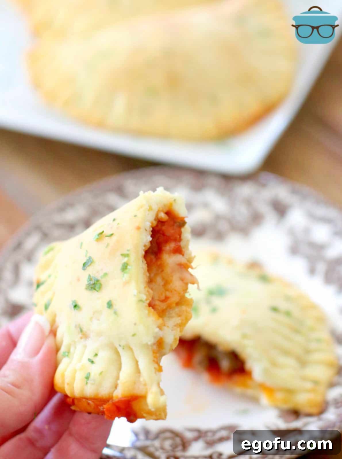 A hand opening a homemade pizza pocket to reveal its delicious, melted cheese, pepperoni, and sausage filling.