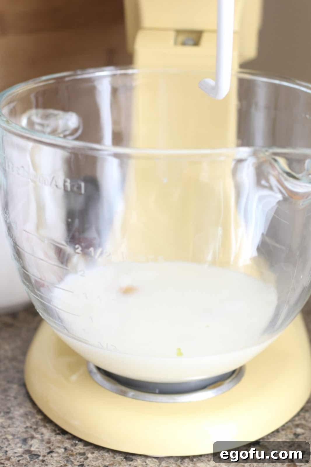 Milk, minced garlic, and eggs are combined in the bottom of a stand mixer bowl, ready to be whisked.