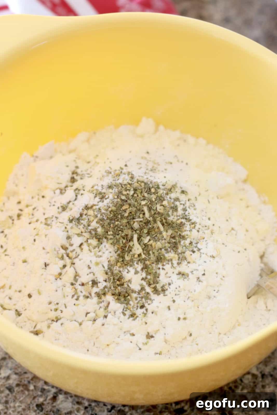 All-purpose flour, grated Parmesan cheese, baking powder, and Italian seasoning in a yellow mixing bowl.
