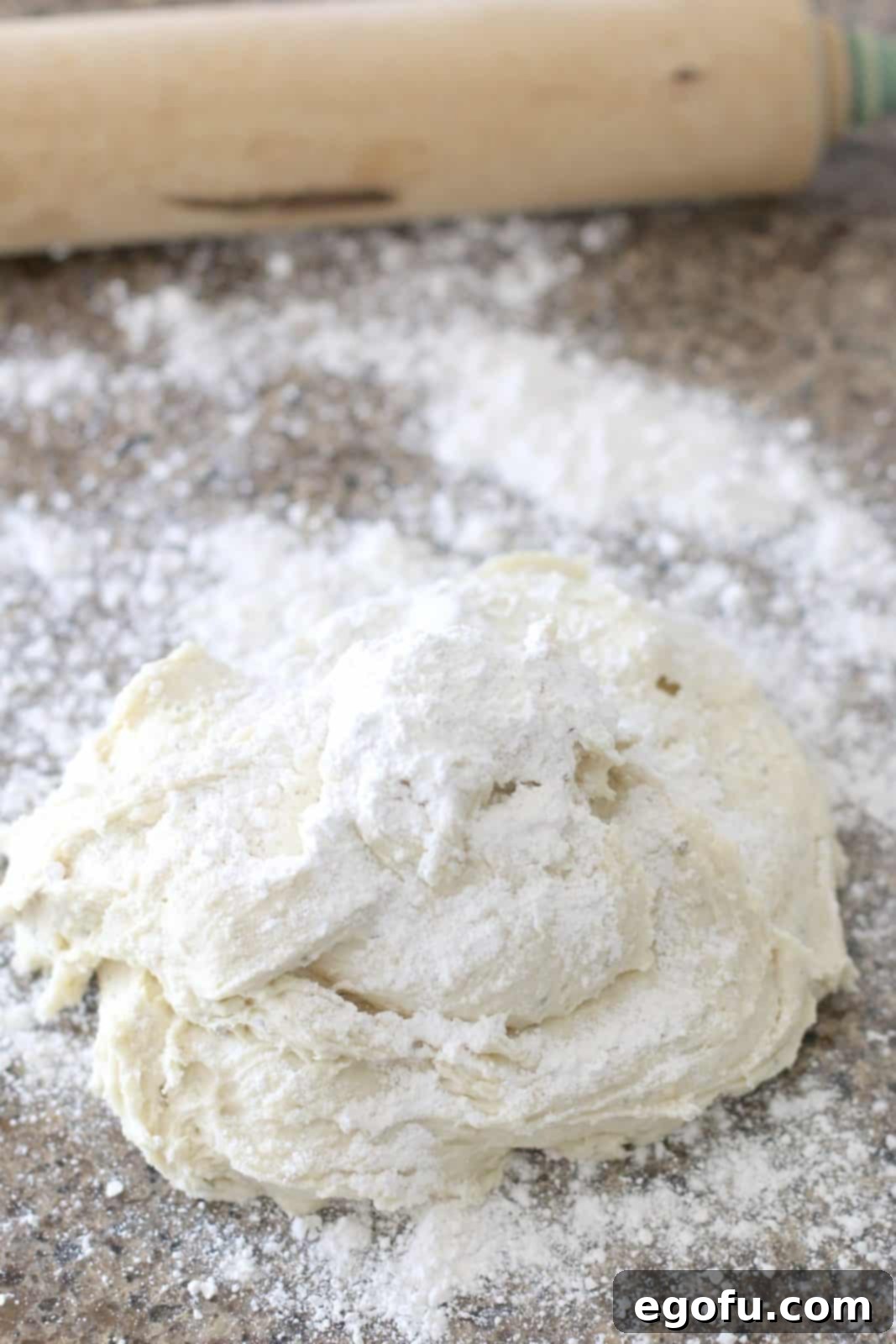 A loose dough ball covered in flour rests on a large, floured countertop.