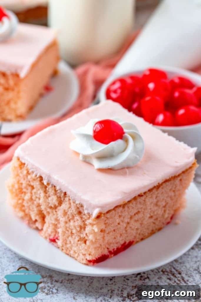 A beautifully sliced Maraschino Cherry Cake on a small white plate, with a bowl of whole maraschino cherries blurred in the background, showcasing the cake's vibrant pink interior and creamy white frosting.