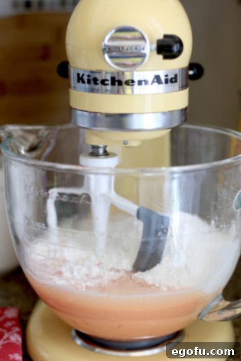 Vanilla cake mix being added to the wet ingredients in a large mixing bowl, ready to be combined into a smooth batter.