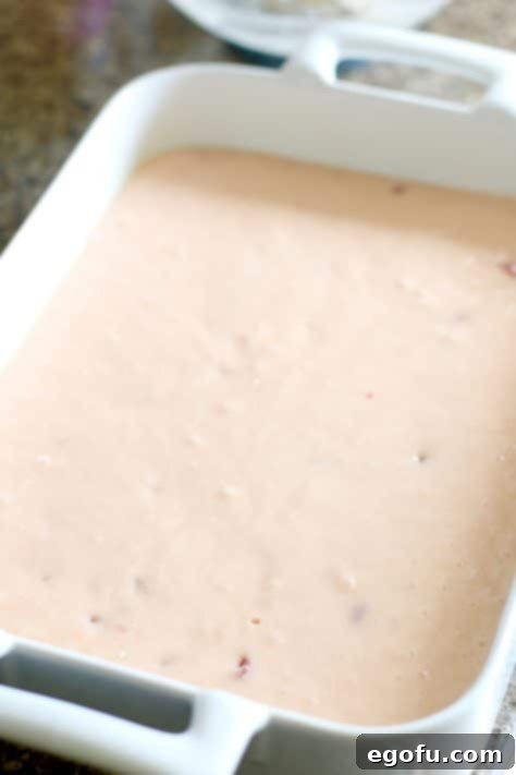 Smooth pink cake batter being poured into a greased 9x13 inch baking dish, ready for the oven.