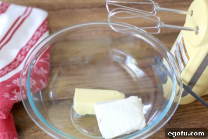 Softened cream cheese and butter creaming together in a mixing bowl with an electric mixer, forming a smooth base for the frosting.