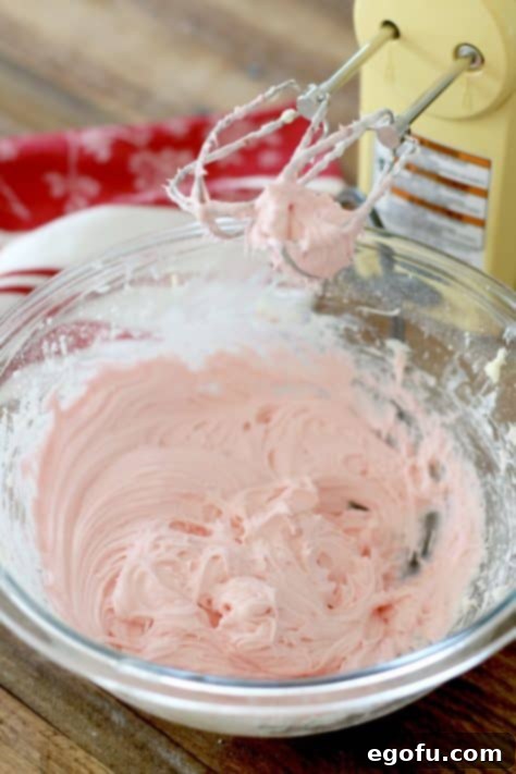 Maraschino cherry juice and almond extract being poured into the nearly finished cream cheese frosting mixture, ready to be blended for flavor and color.