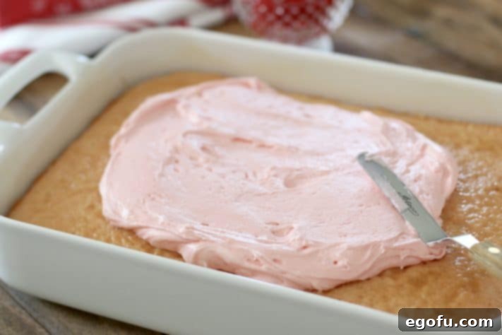 A vibrant pink frosting being smoothly spread over the surface of a cooled cake in a baking dish, creating an even layer.
