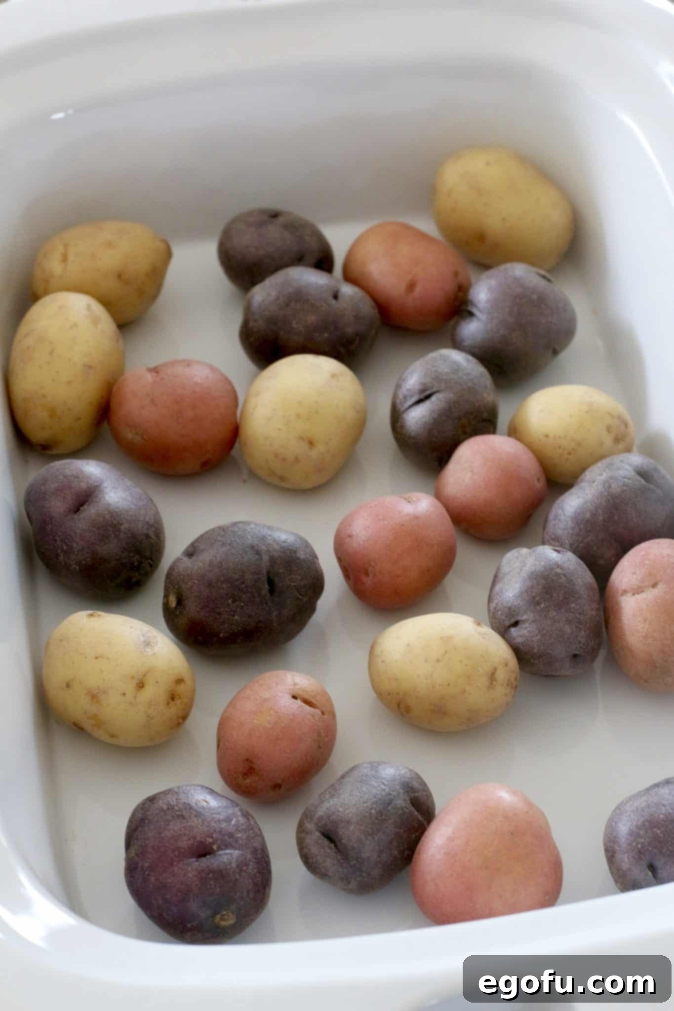 Easy Slow Cooker Creamy Sausage and Potatoes 4 Uncooked Little Potatoes placed neatly at the bottom of a slow cooker.