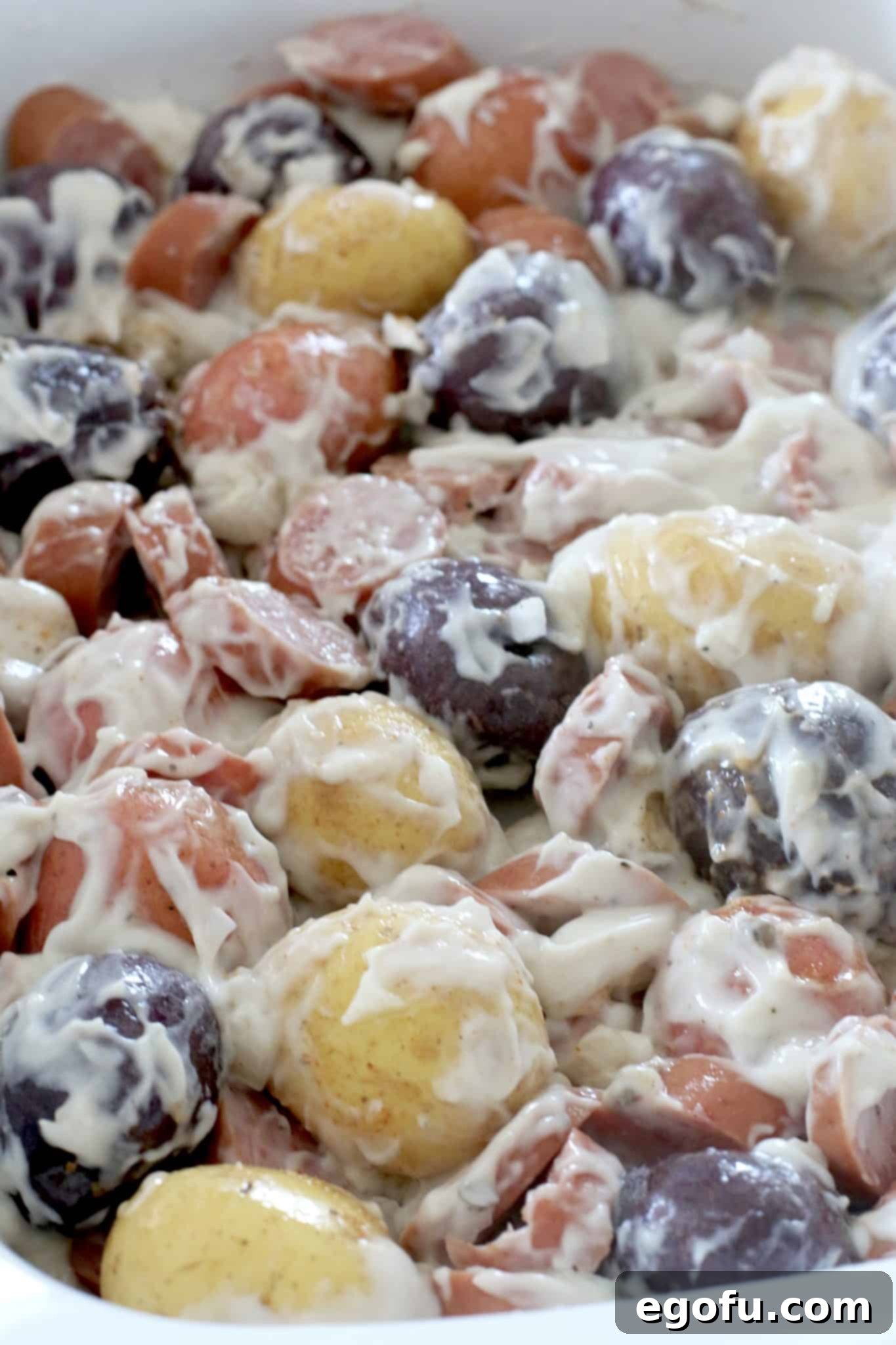 Easy Slow Cooker Creamy Sausage and Potatoes 7 Cream of mushroom soup spread over potatoes and sausage in a slow cooker, ready to be stirred.