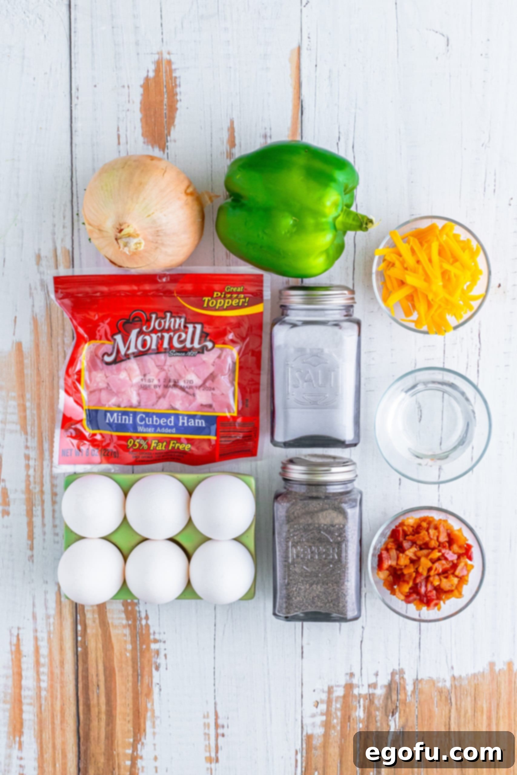 Your Instant Mug Omelet 4 A vibrant array of fresh ingredients for a Microwave Omelet in a Mug: eggs, chopped onion, green bell pepper, salt, pepper, crispy bacon, shredded cheddar cheese, and diced ham, beautifully arranged.