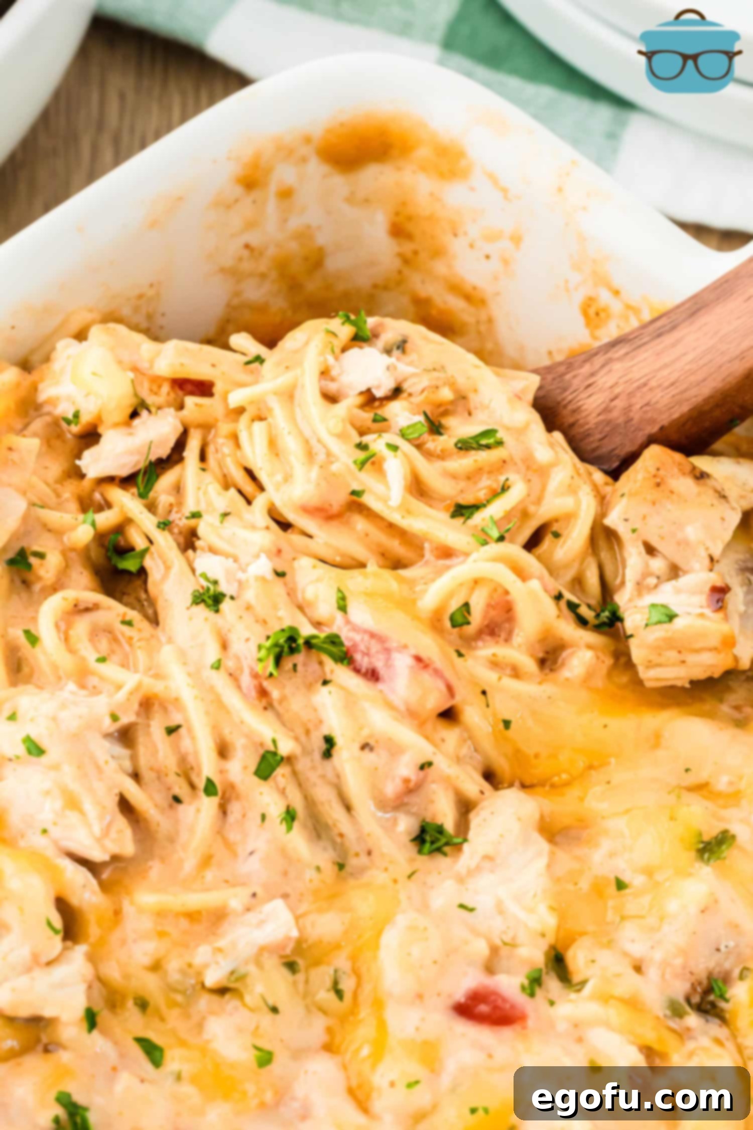 Looking down on a casserole dish with a serving utensil getting a scoop of Chicken Spaghetti, showcasing its creamy texture and golden-brown top.