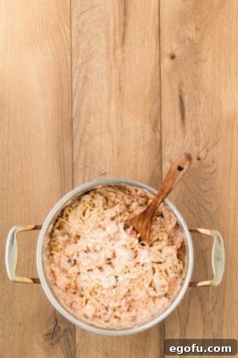 Chicken, pasta, and sauce mixture being stirred in a large pot.