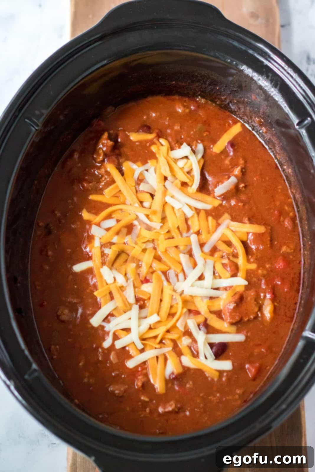 Finished Slow Cooker Ultimate Beef Chili, generously topped with shredded cheese, ready to be served directly from the slow cooker.