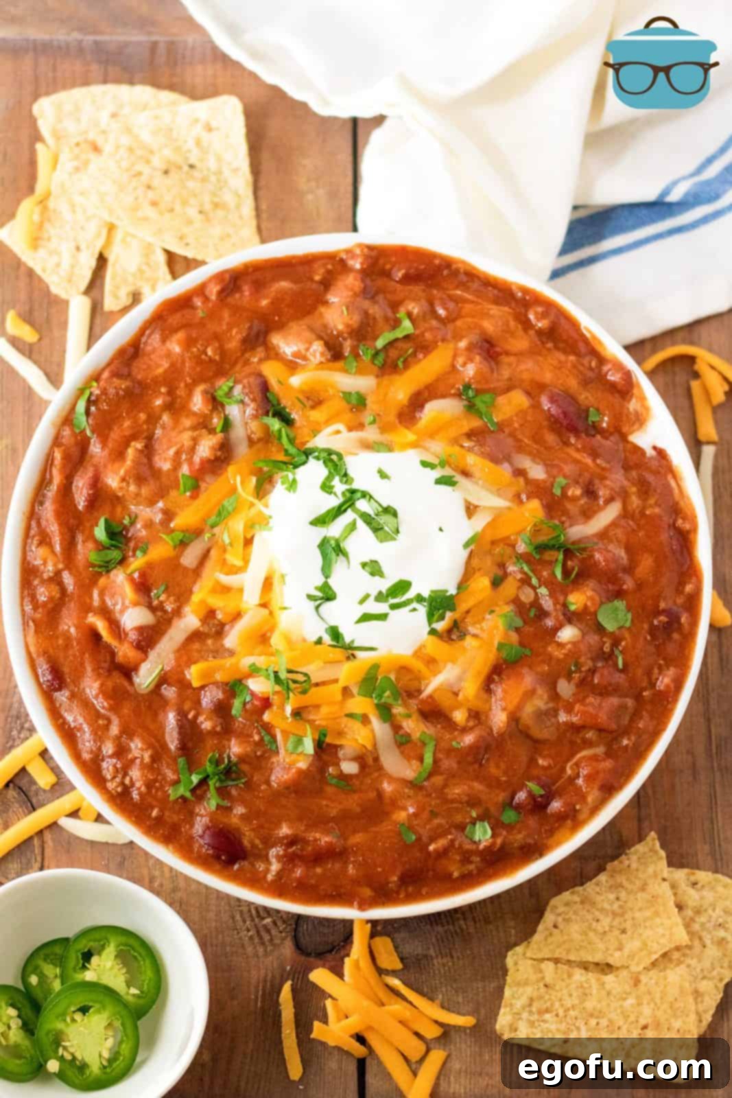 Overhead shot of a garnished bowl of Slow Cooker Ultimate Beef Chili, topped with cheese and fresh herbs, ready to be served.