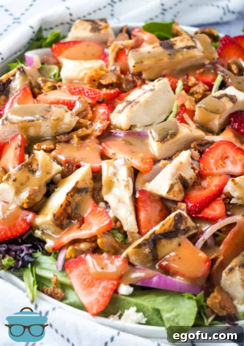 Strawberry Fields Salad, a vibrant mix of greens, strawberries, chicken, and nuts, drizzled with balsamic dressing in a white bowl.