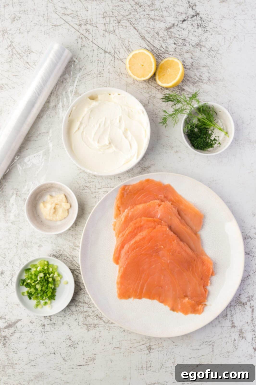 A vibrant flat lay of all the essential ingredients needed for Salmon Pinwheels: smoked salmon, softened cream cheese, creamy horseradish sauce, fresh dill, spring onions, lemon, and a pepper mill.