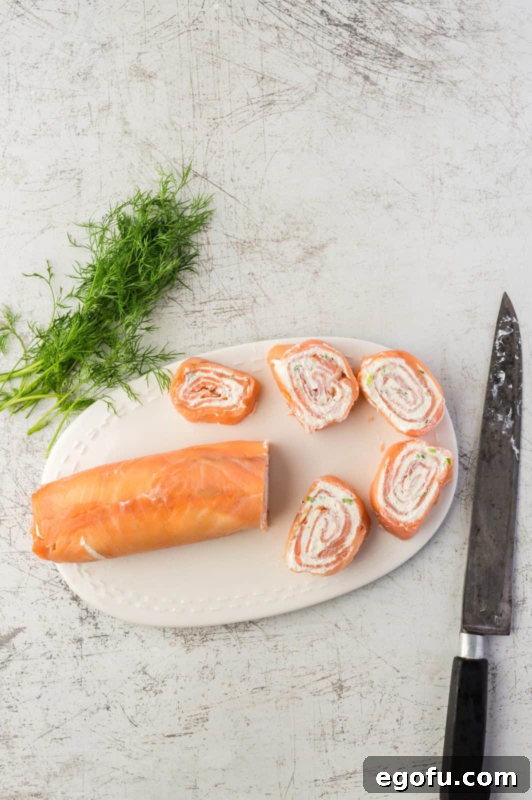 A close-up view of a sharp knife carefully slicing the chilled salmon log into individual, perfectly spiraled pinwheels.