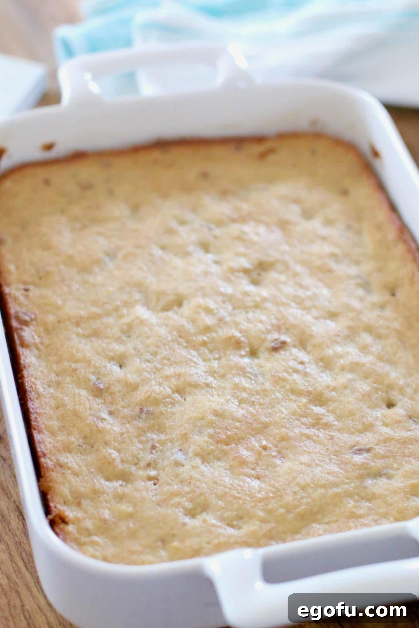 A sheet cake of Hummingbird Bars cooling in a white ceramic baking dish on a wire rack.