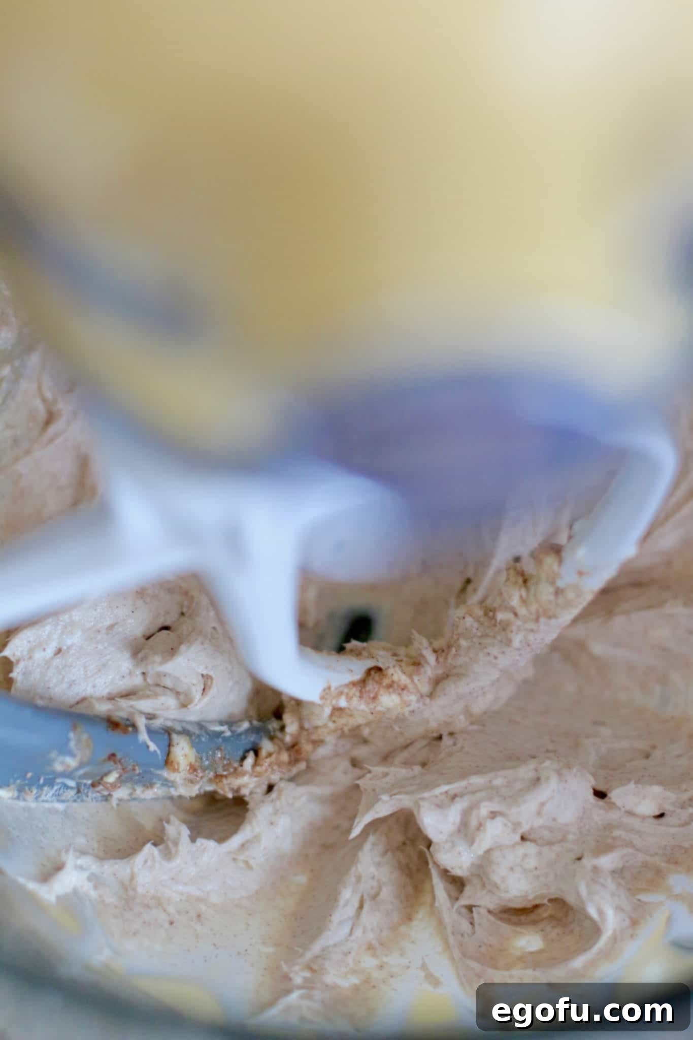 Softened cream cheese, butter, ground cinnamon, and vanilla extract being beaten together in a clear KitchenAid stand mixer bowl for the homemade frosting.