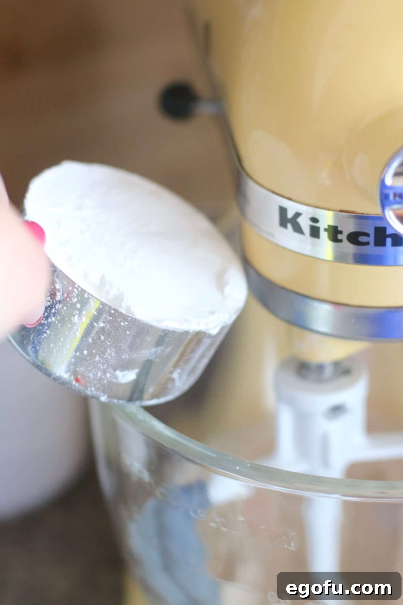 Powdered sugar being gradually added to the cream cheese, butter, and spice mixture for a smooth frosting.