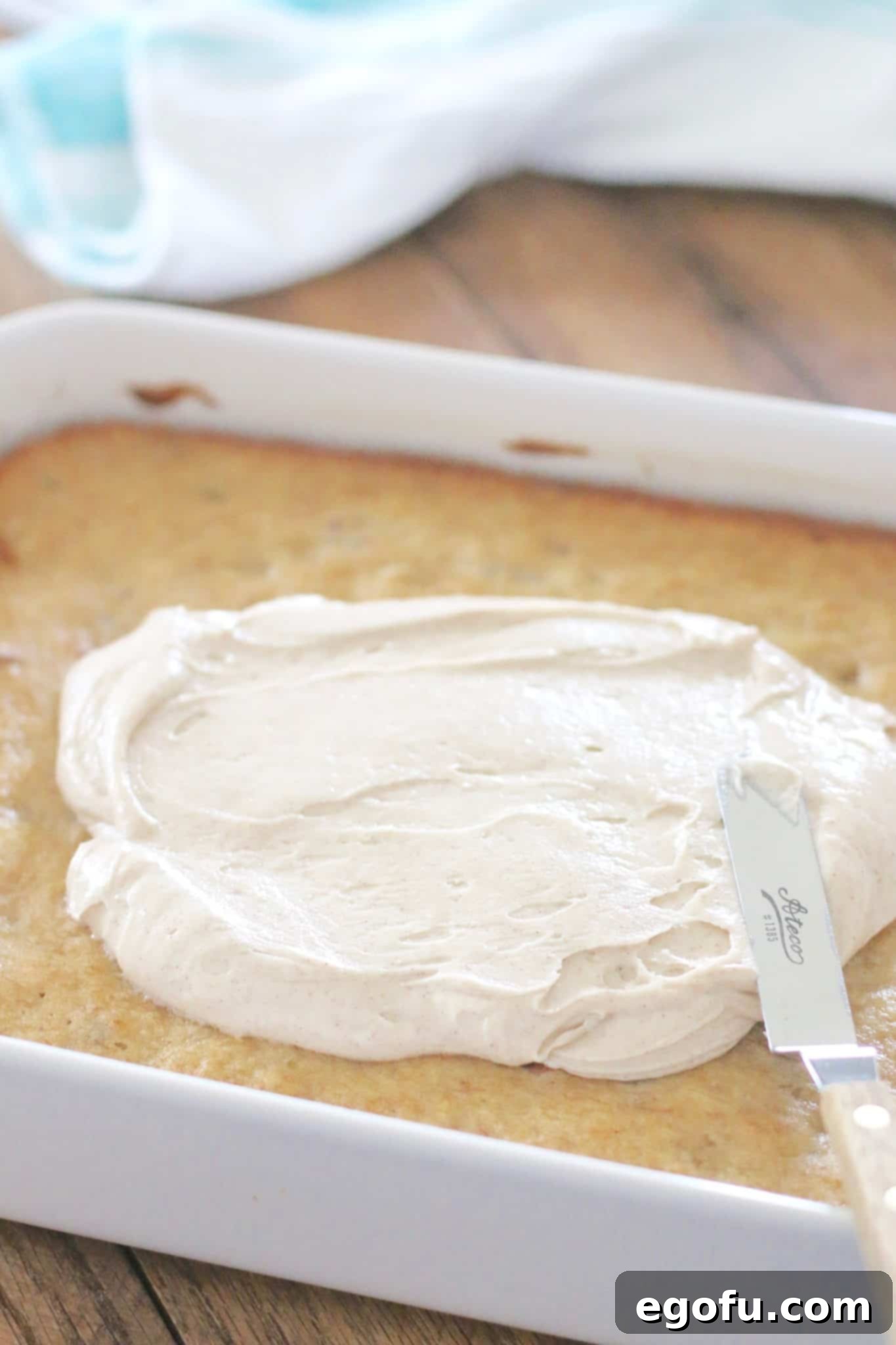 Homemade Cinnamon Cream Cheese Frosting being expertly spread evenly on the cooled Hummingbird Cake Bars using an offset spatula.