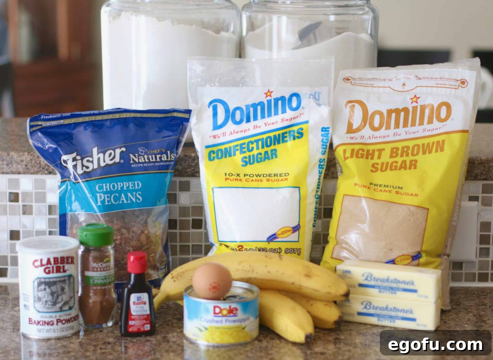 A vibrant display of key ingredients for Hummingbird Cake Bars: chopped pecans, mashed ripe bananas, drained crushed pineapple, softened butter, light brown sugar, confectioners sugar, ground cinnamon, and fragrant vanilla extract.