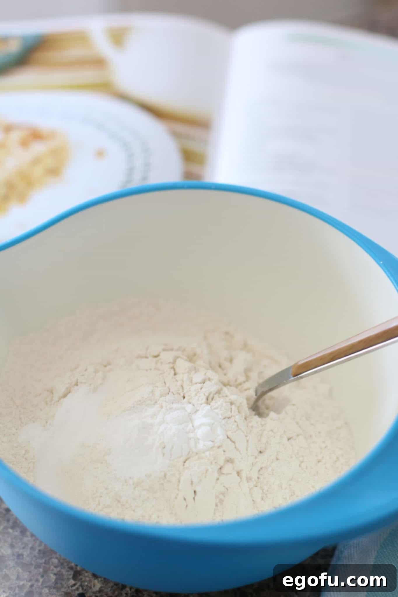 Dry ingredients for Hummingbird Cake Bars, including flour, baking powder, and salt, being stirred together in a blue bowl with a fork.