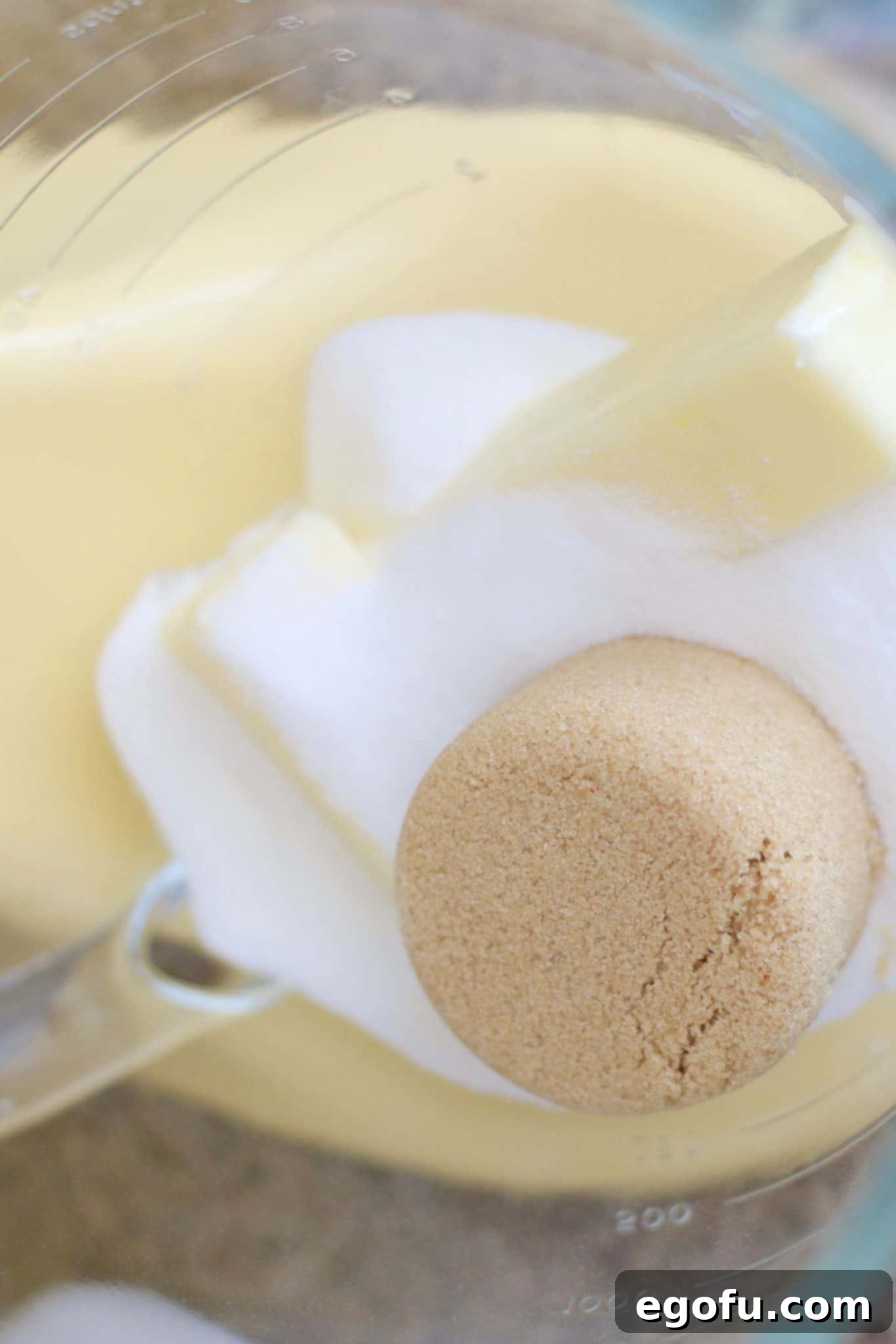 Softened unsalted butter, granulated sugar, and light brown sugar being creamed in the clear bowl of a yellow KitchenAid stand mixer.