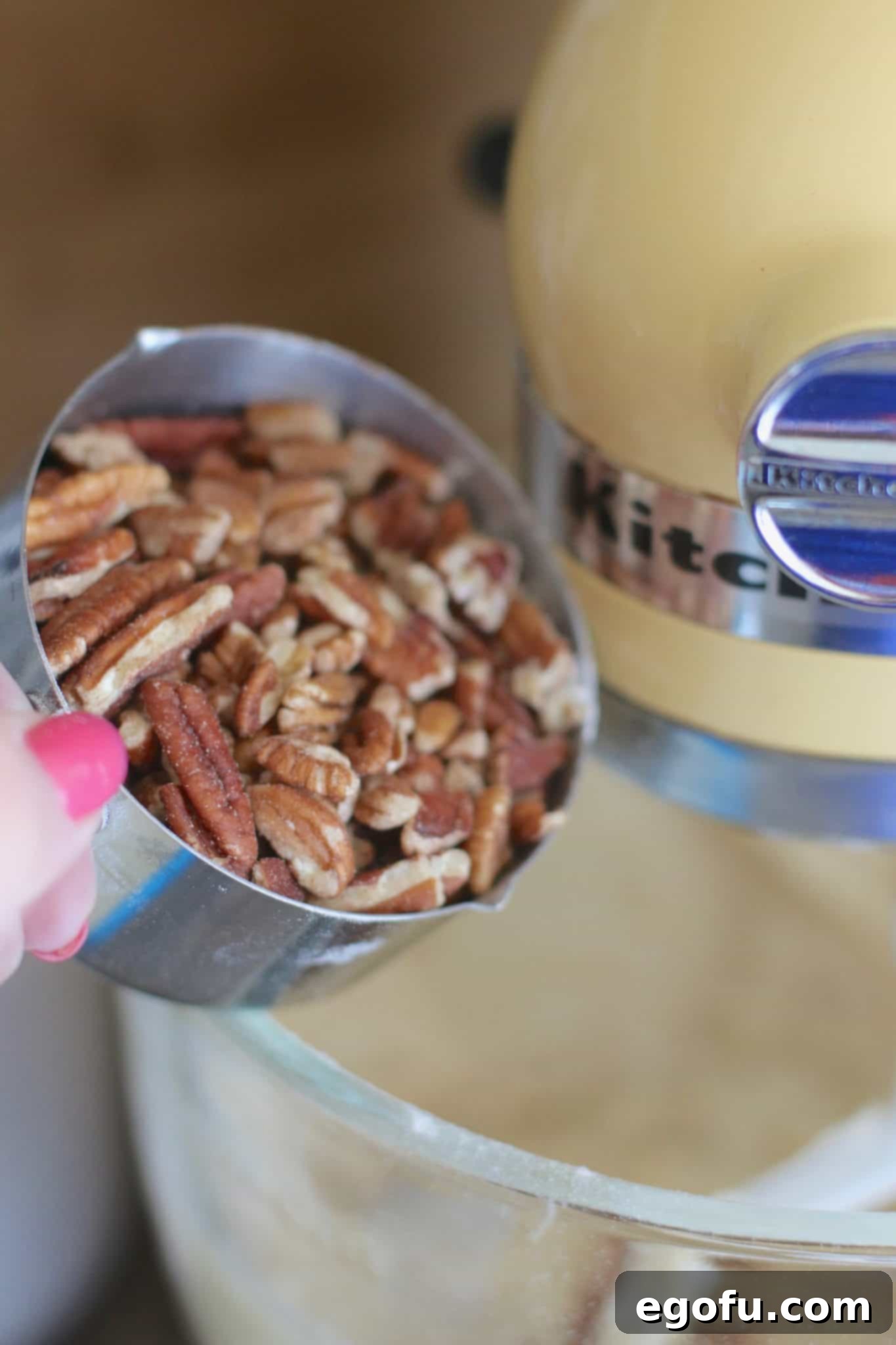 Chopped pecans being carefully folded into the hummingbird cake batter with a spatula.