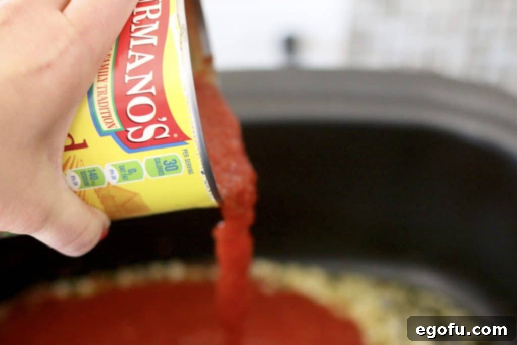 Slow Simmered Homemade Meatballs with Zesty Marinara 7 pouring crushed tomatoes into the bottom of a slow cooker along with olive oil and crushed garlic
