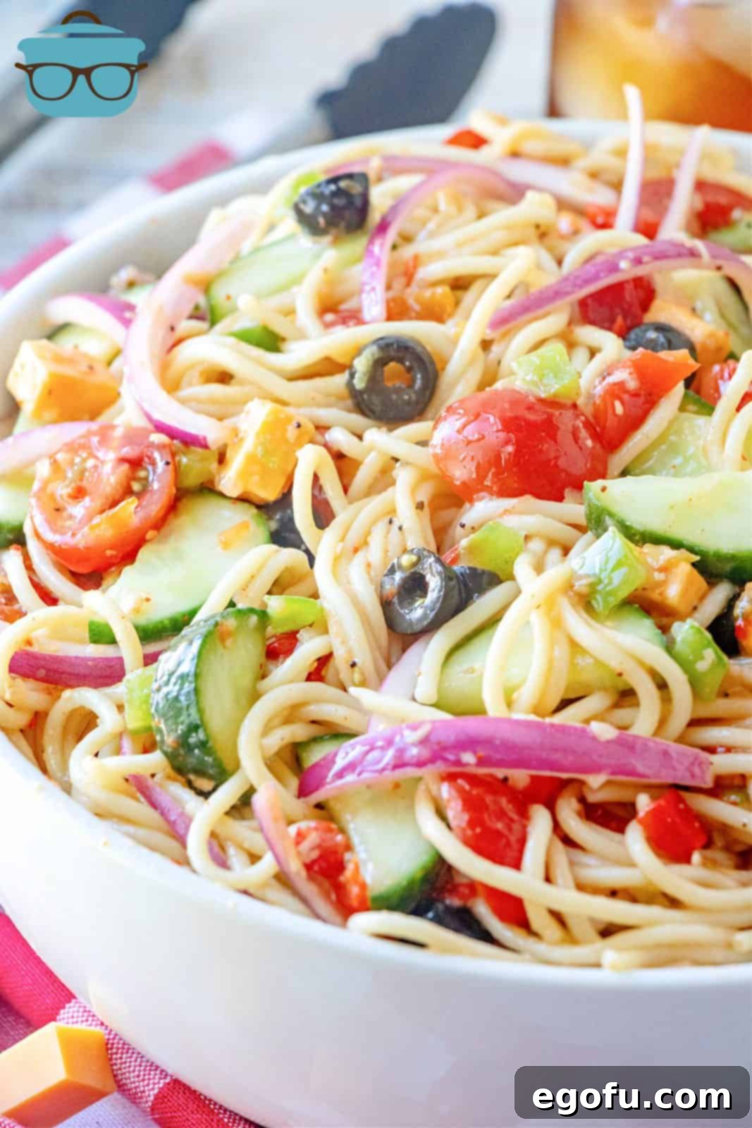 Close-up photo of a vibrant Summer Spaghetti Salad in a large white serving bowl, showcasing fresh vegetables and cheese.