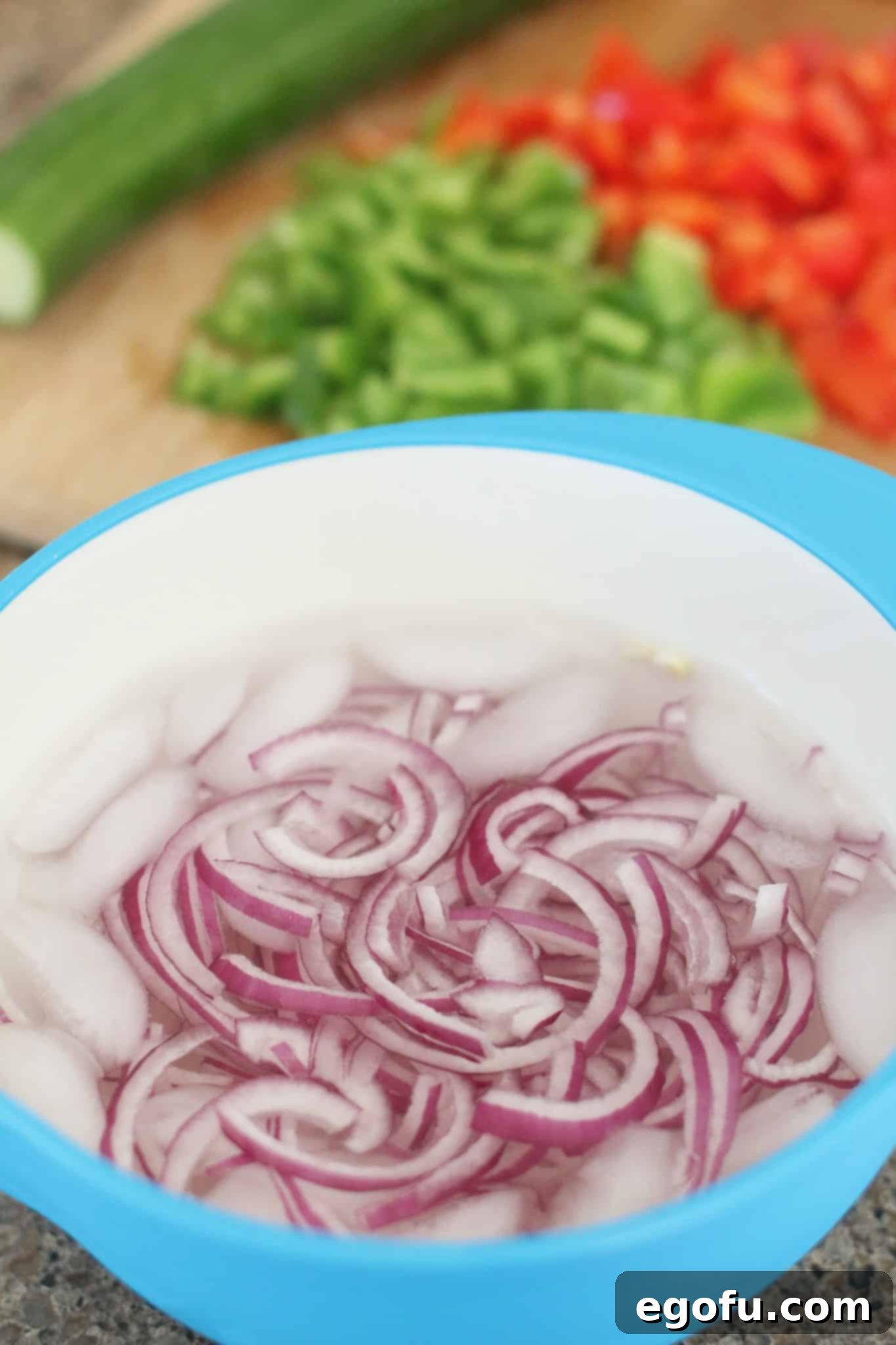 Thinly sliced red onions soaking in a bowl of ice water, a clever tip to reduce their strong flavor for raw dishes.