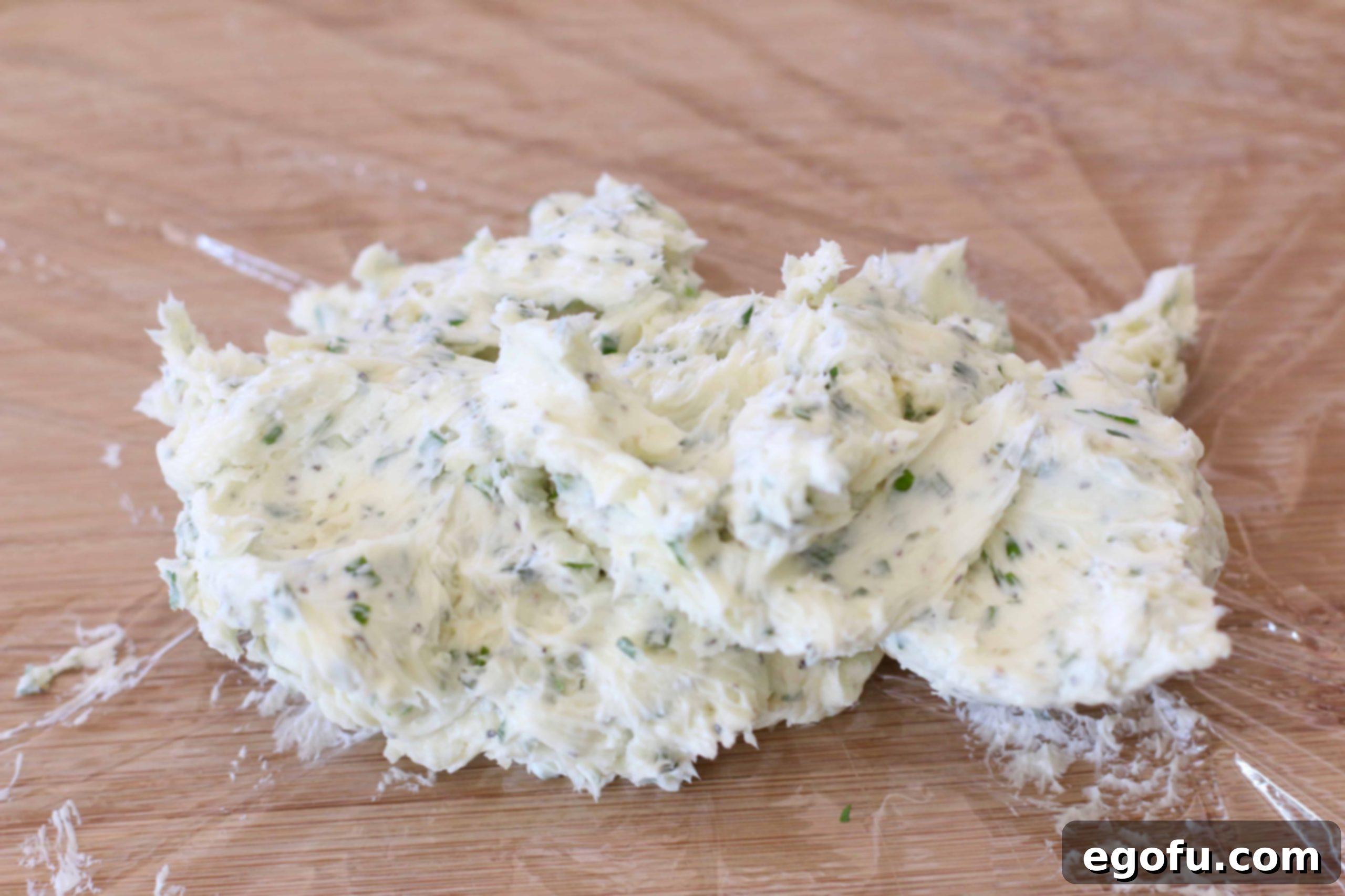 The compound butter has been rolled into a log shape and wrapped in plastic wrap.