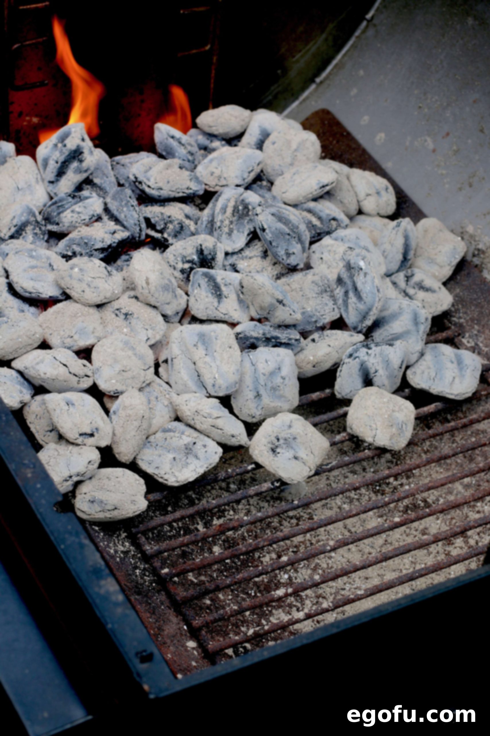 Glowing charcoal briquets have turned mostly gray, indicating optimal heat for grilling.