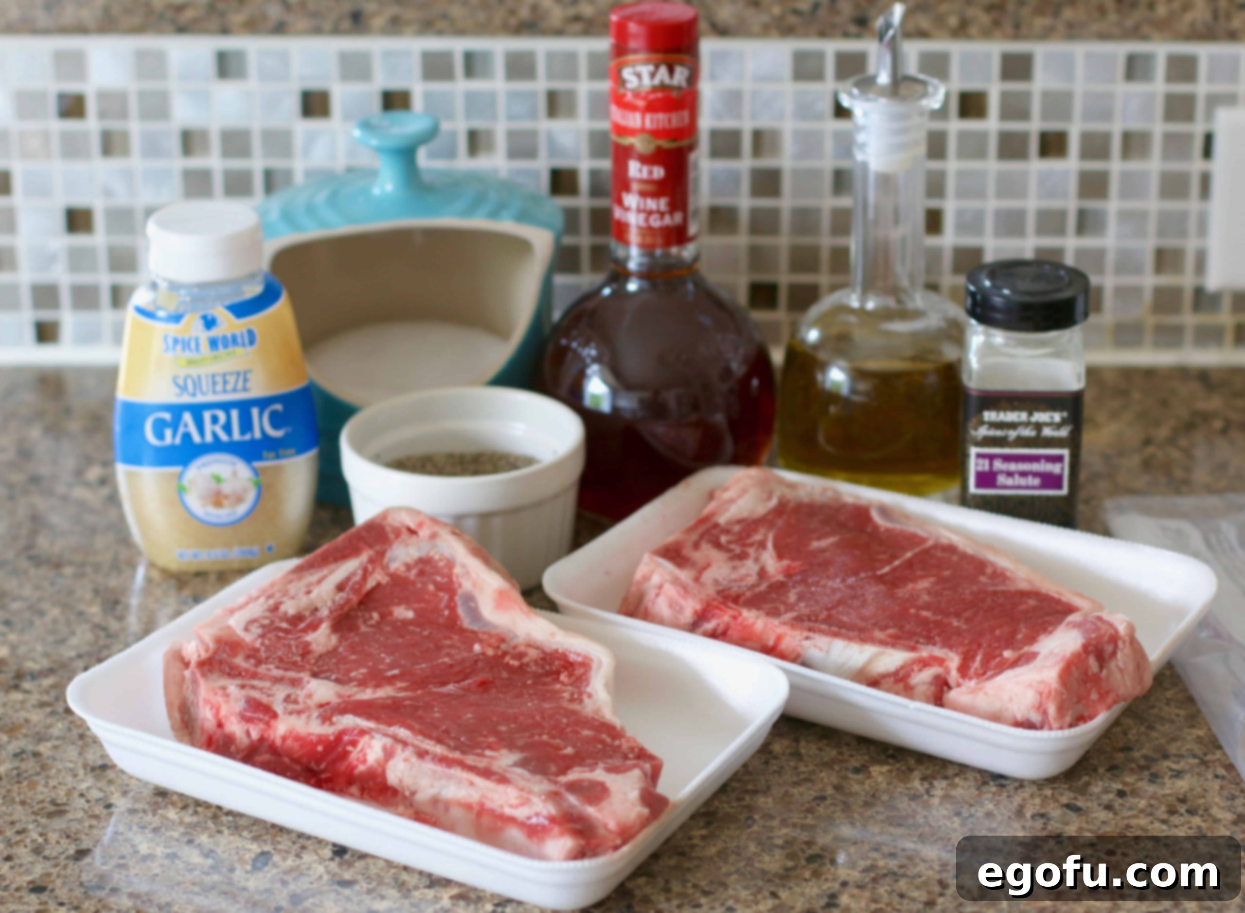 A selection of marinade ingredients including extra virgin olive oil, red wine vinegar, 21 seasoning salute, minced garlic, kosher salt, and black pepper arranged on a cutting board.