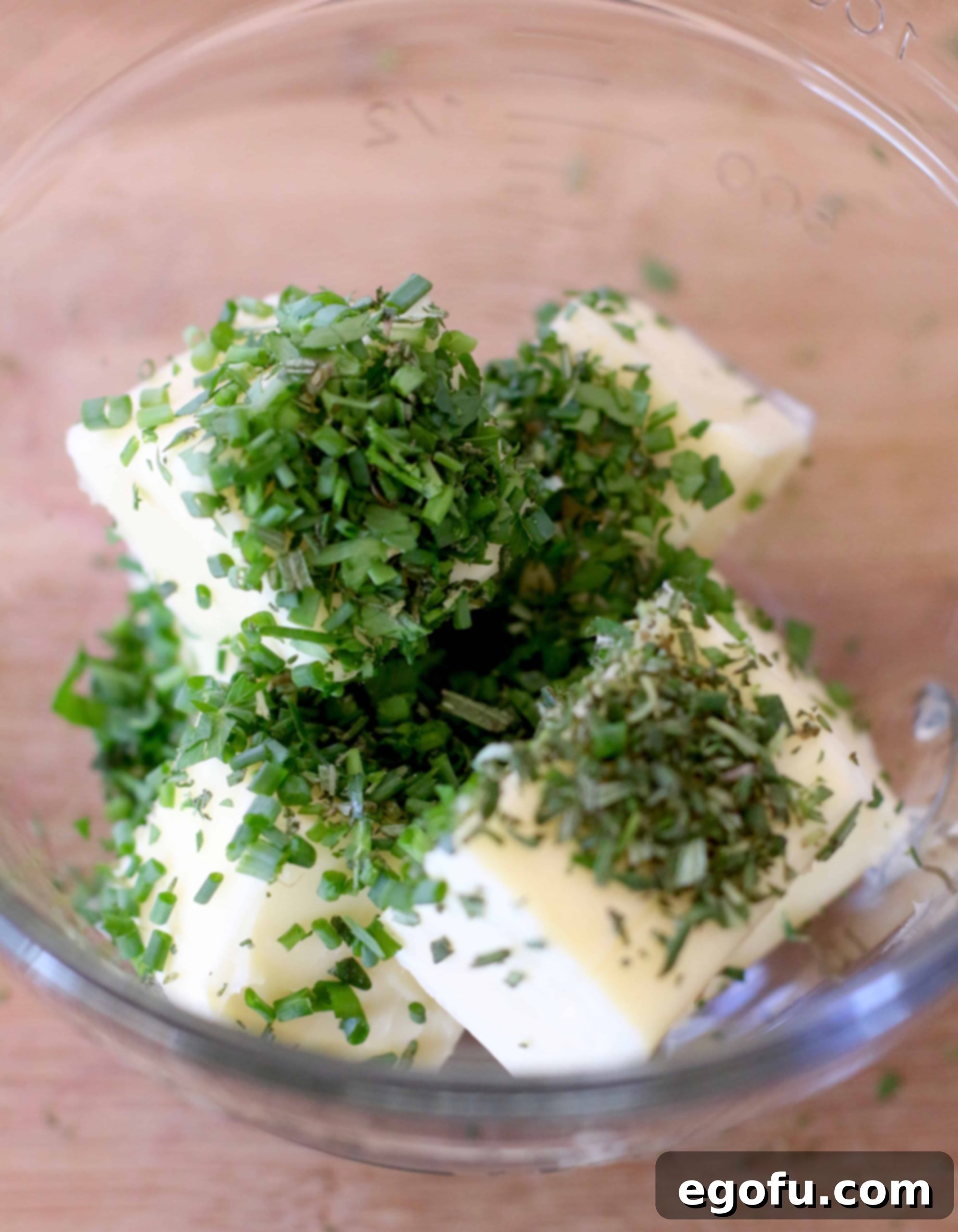Softened butter being mixed with finely chopped fresh herbs in a bowl.