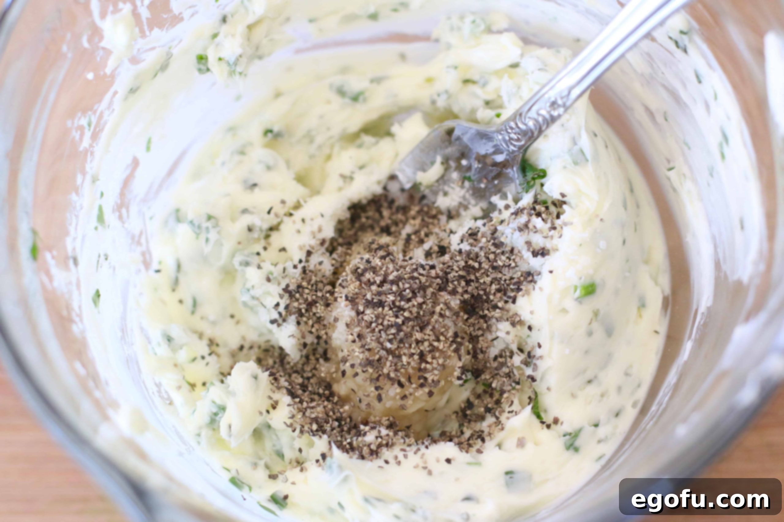 Compound butter mixture with salt, pepper, minced garlic, and fresh herbs, ready to be shaped.