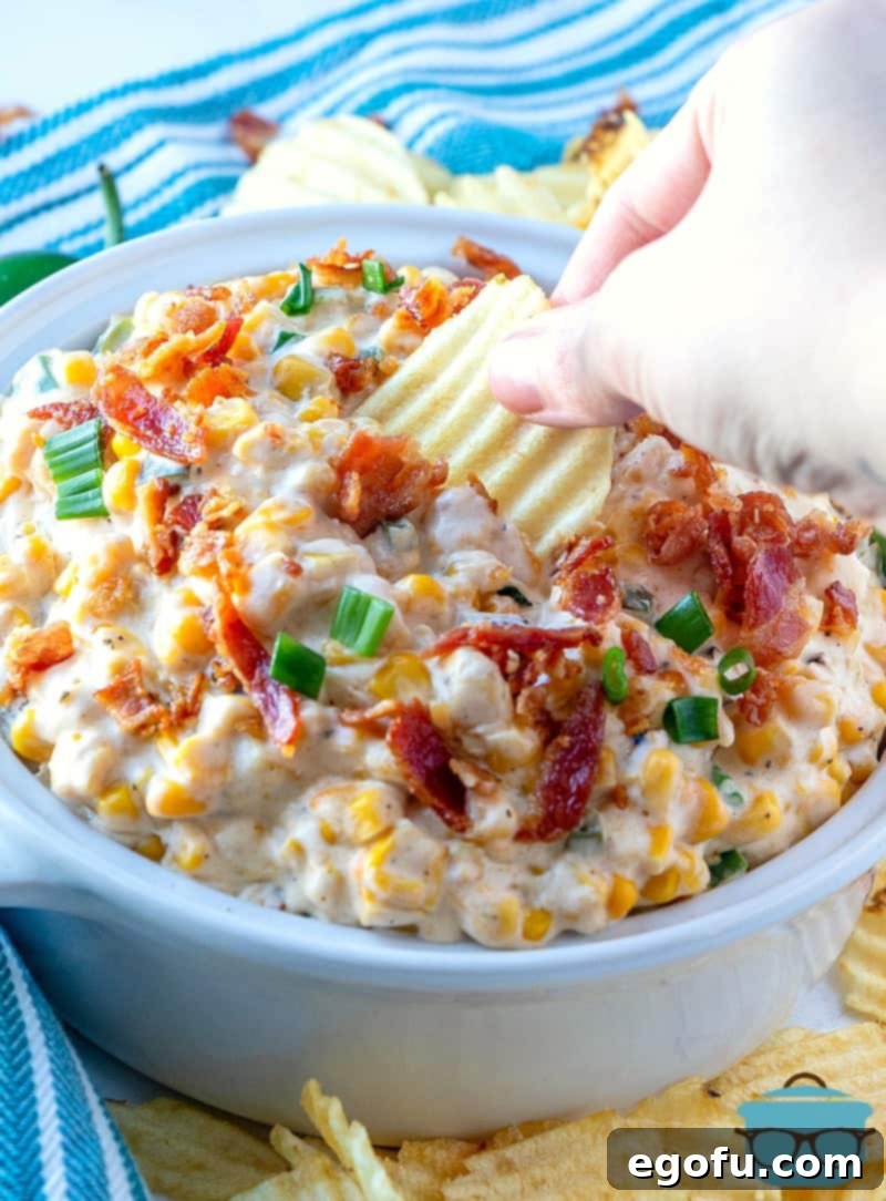 Jalapeno Popper Corn Dip served in a white serving bowl with a tortilla chip dipped in, showcasing its creamy texture.