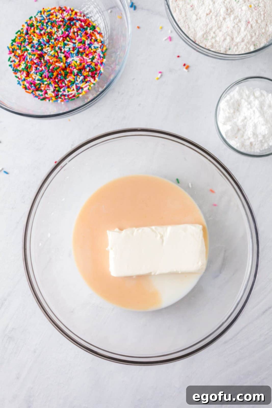 Confetti Cake Bliss 5 Cream cheese, milk, and vanilla extract are being mixed together in a bowl until smooth.