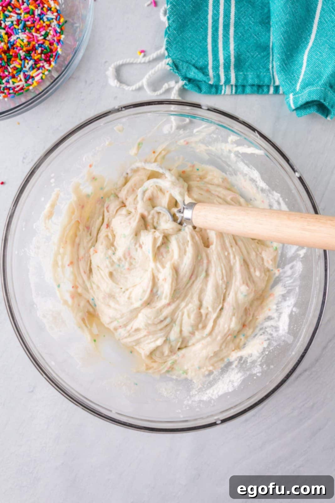 Confetti Cake Bliss 7 The cake batter dip mixture is being folded and whisked in a bowl to achieve a smooth and consistent texture.