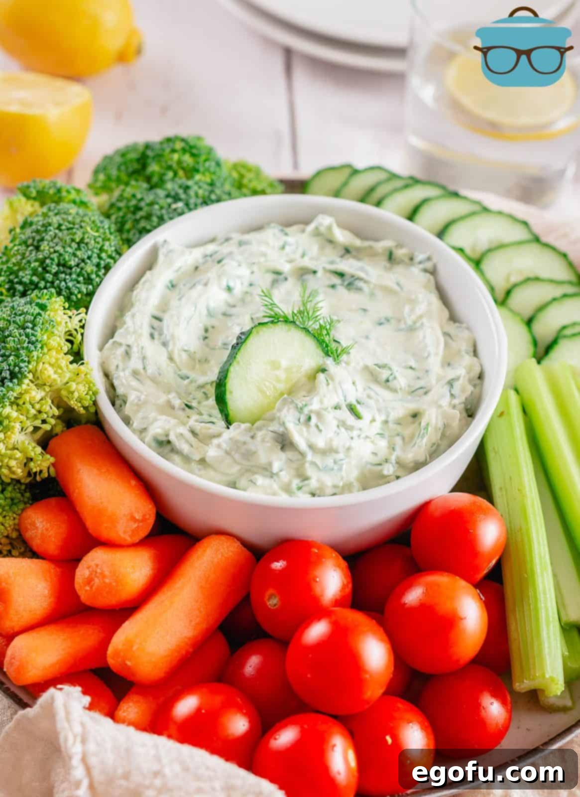 Chilled Garden Spinach Dip 2 Creamy Spinach Dip presented in a rustic white bowl, artfully surrounded by an assortment of vibrant, fresh vegetables including cucumber slices, carrot sticks, and bell pepper strips, perfect for dipping.